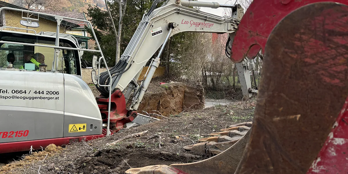 Ein Bagger führt Baggerarbeiten aus, um einen Baumstumpf aus einem mit Laub und spärlichem Gras bedeckten Gelände zu entfernen.