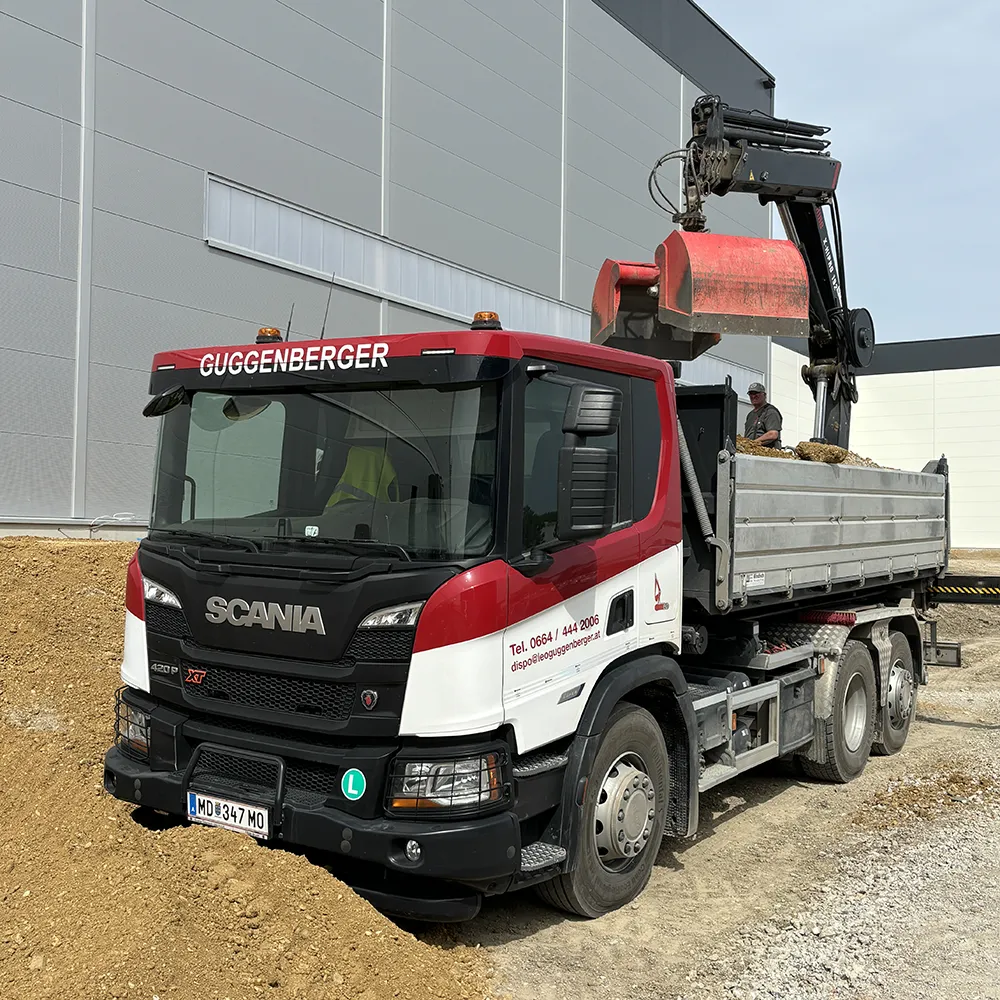 Ein Bagger führt Baggerarbeiten aus, um einen Baumstumpf aus einem mit Laub und spärlichem Gras bedeckten Gelände zu entfernen.